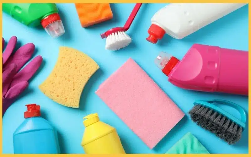 A colourful arrangement of cleaning supplies, including sponges, brushes, and various bottles, on a bright blue background.