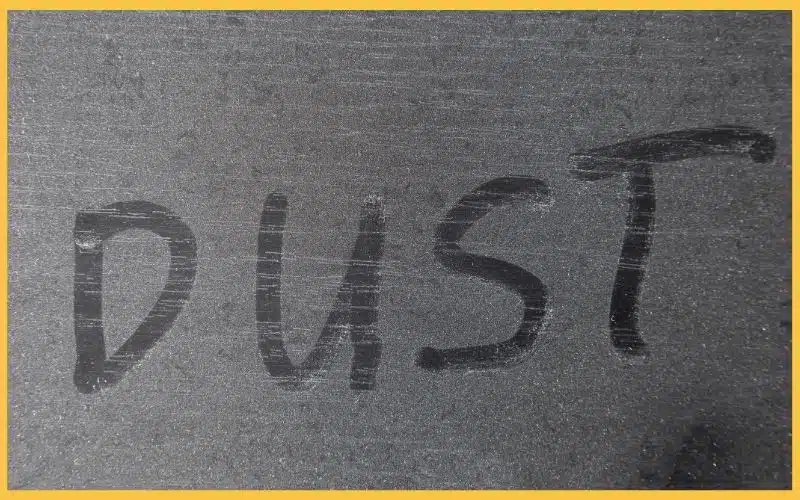 The word "DUST" is written in smudged letters on a dark, dusty surface.