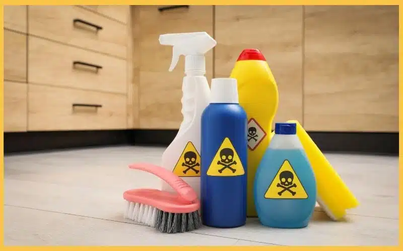 A collection of cleaning products with hazard symbols, including sprays and bottles, arranged on a kitchen floor.