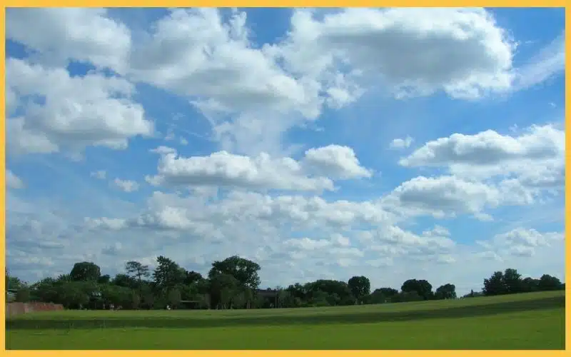 A serene landscape featuring a vibrant green field under a bright blue sky filled with fluffy white clouds.