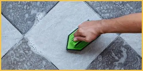 A hand brushing a floor with soap bubbles.