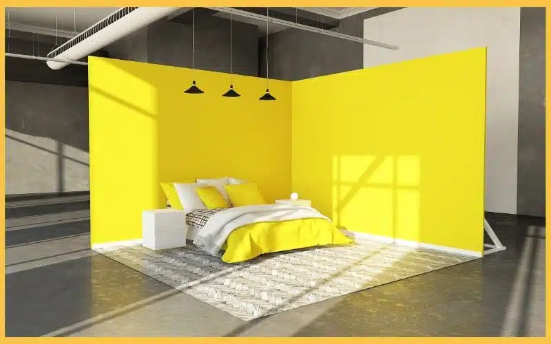 Bright yellow walls enclose a cozy bedroom with a white bed, colorful pillows, and a patterned rug, under modern pendant lighting.