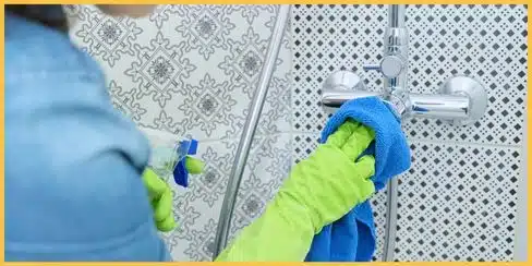 Professional cleaning service wiping a shower faucet.