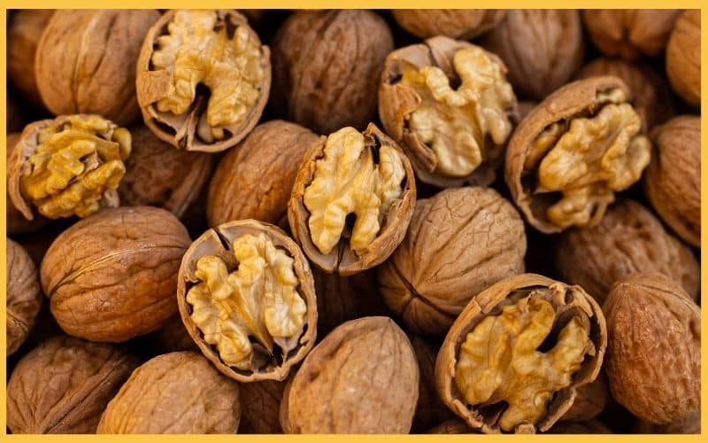 A close-up of cracked and whole walnuts, showcasing their rich, golden interiors against a background of brown shells.
