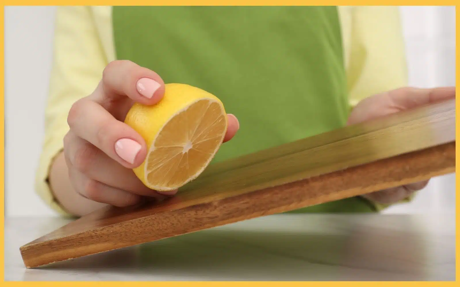 A hand holding a halved lemon above a wooden cutting board, set against a light-colored background.