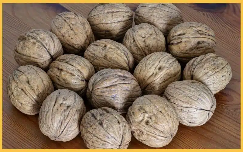 A cluster of whole, cracked walnuts arranged on a wooden surface, displaying their rough, textured shells.