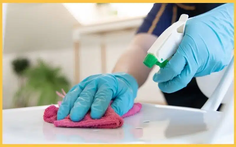 A gloved hand wiping a surface while the other hand holds a cleaning spray bottle.