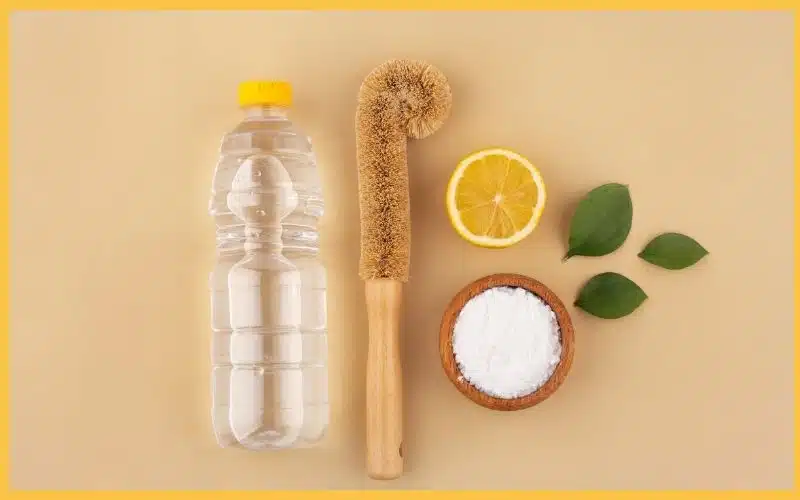A surface with a cleaning brush, lemon, baking soda, and water placed together to represent natural cleaning.