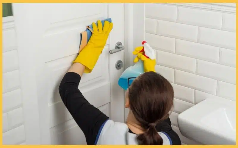 A cleaning professional wiping a door using a microfiber cloth while holding a cleaning spray.