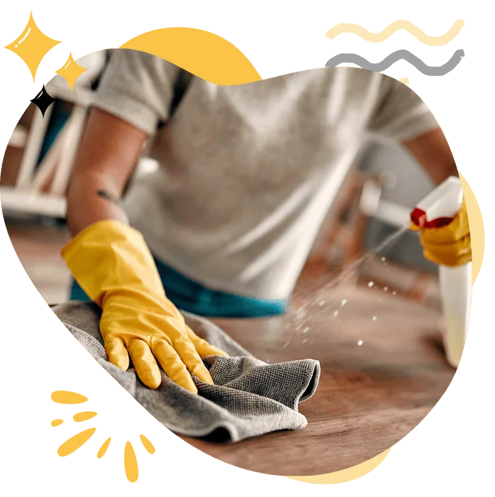A person wearing yellow cleaning gloves sprays a cleaning solution while wiping a surface with a cloth, showcasing deep cleaning services by Hellamaid Canada for homes and offices.