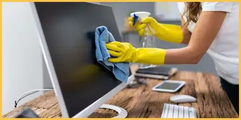 A Canadian professional cleaner wiping a computer screen in a home office.