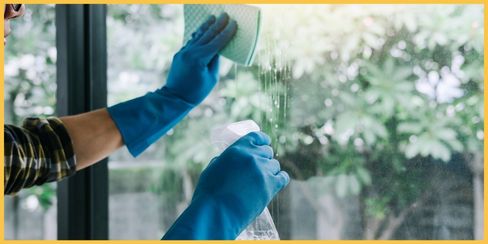 A cleaning professional in Kitchener using a microfiber cloth and spray to clean a window.