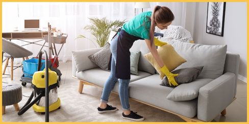 A cleaning professional in Canada arranging pillows neatly on a couch.