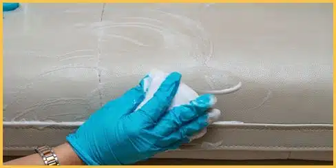 Gloved hands cleaning leather with visible bubbles from a cleaning solution.