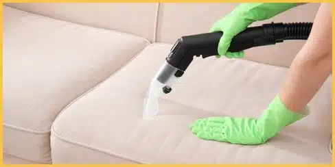 Gloved hands vacuuming a sofa.