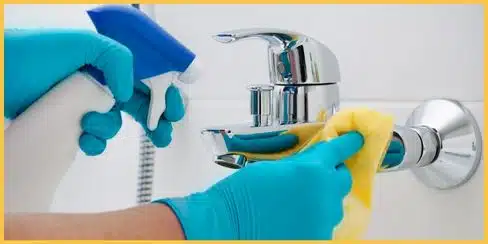 Gloved hands cleaning a bathroom faucet.
