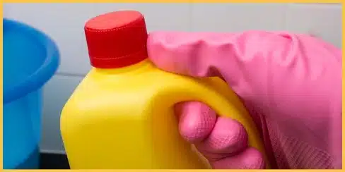 Gloved hand holding a bottle of bleach cleaner.