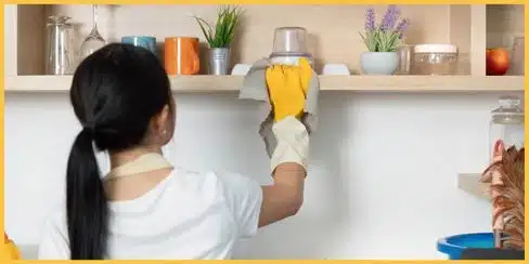 A lady that's cleaning a kitchen shelve.